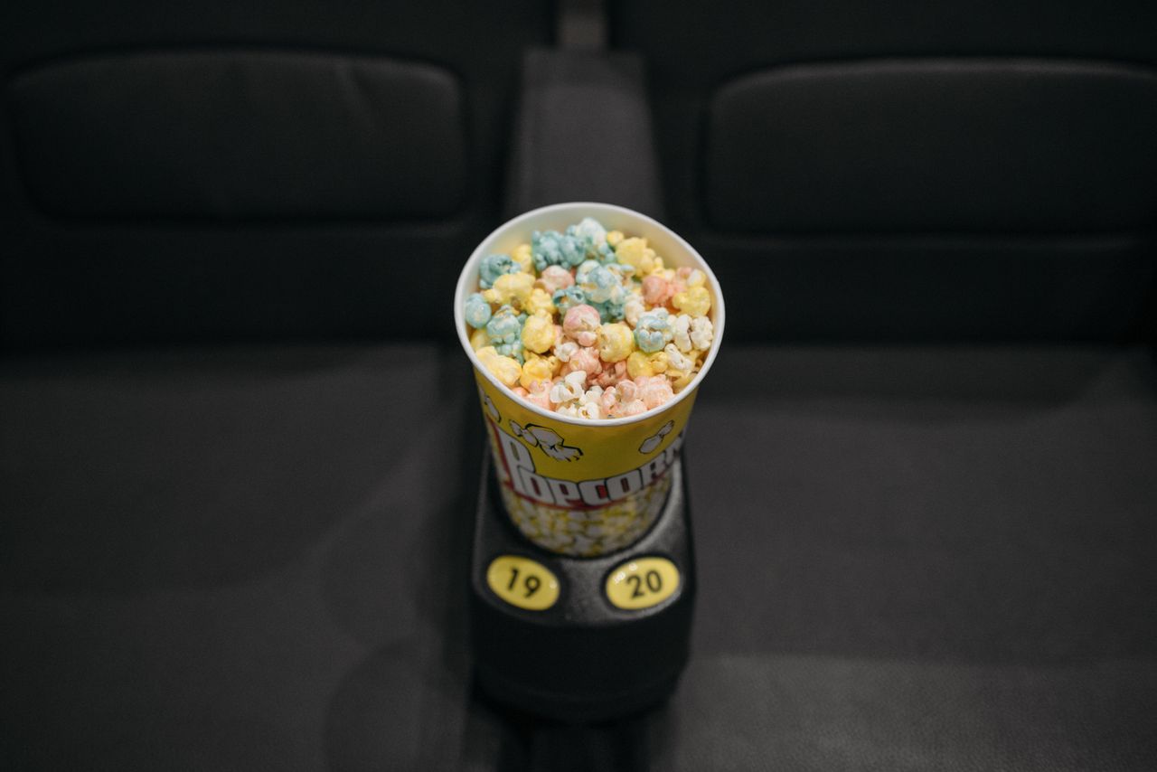 A tub of colorful popcorn resting on a seat armrest in a movie theater.