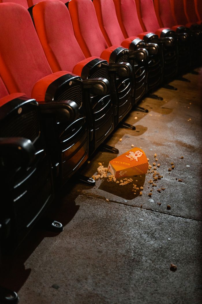 A movie theatre scene with spilled popcorn on the floor beside red seats. Captures the essence of cinema snacks.